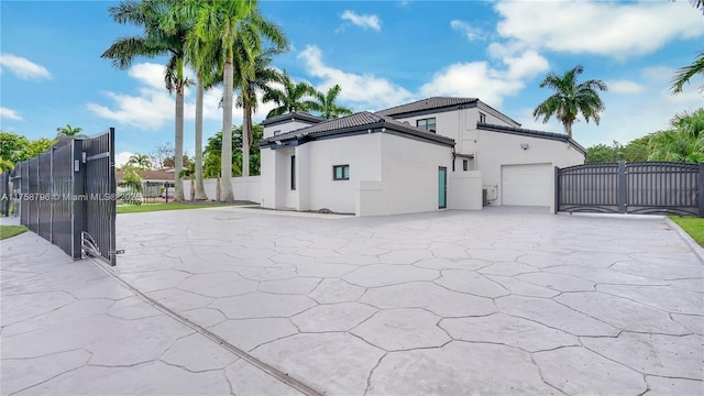 exterior space featuring driveway, an attached garage, a gate, fence, and stucco siding