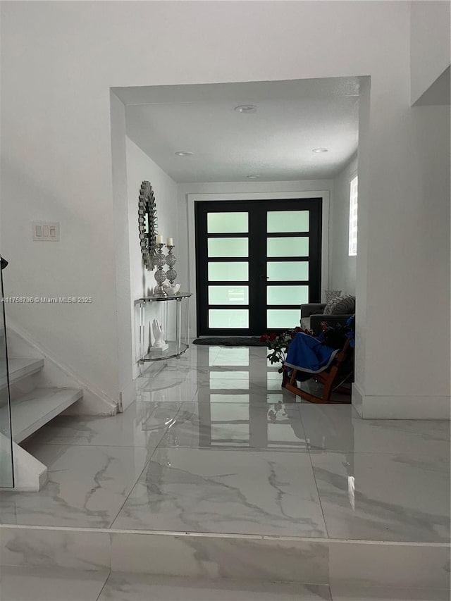 foyer with marble finish floor, stairs, and baseboards