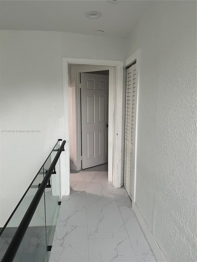 hall with marble finish floor, a textured wall, and an upstairs landing