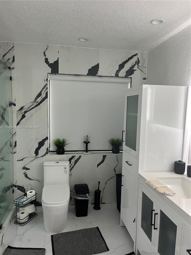 full bath with a textured ceiling, vanity, a marble finish shower, and toilet