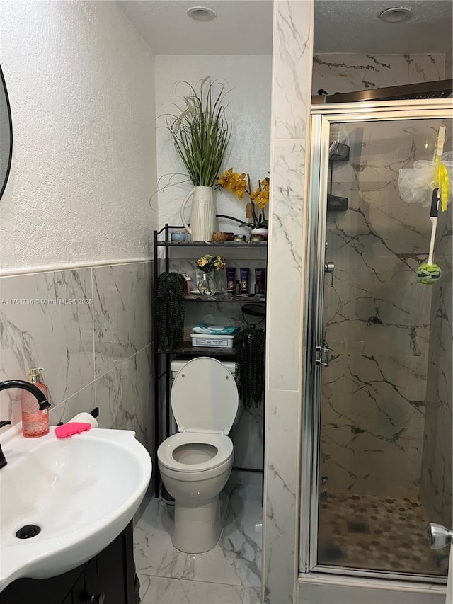 full bath featuring a textured wall, toilet, vanity, marble finish floor, and a marble finish shower