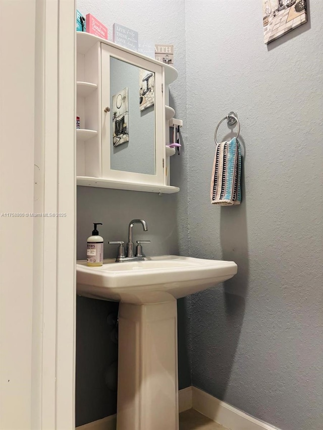 bathroom with baseboards, a sink, and a textured wall