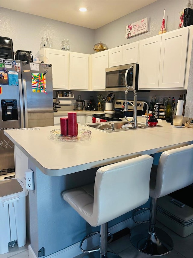 kitchen with appliances with stainless steel finishes, light countertops, white cabinets, and a breakfast bar area