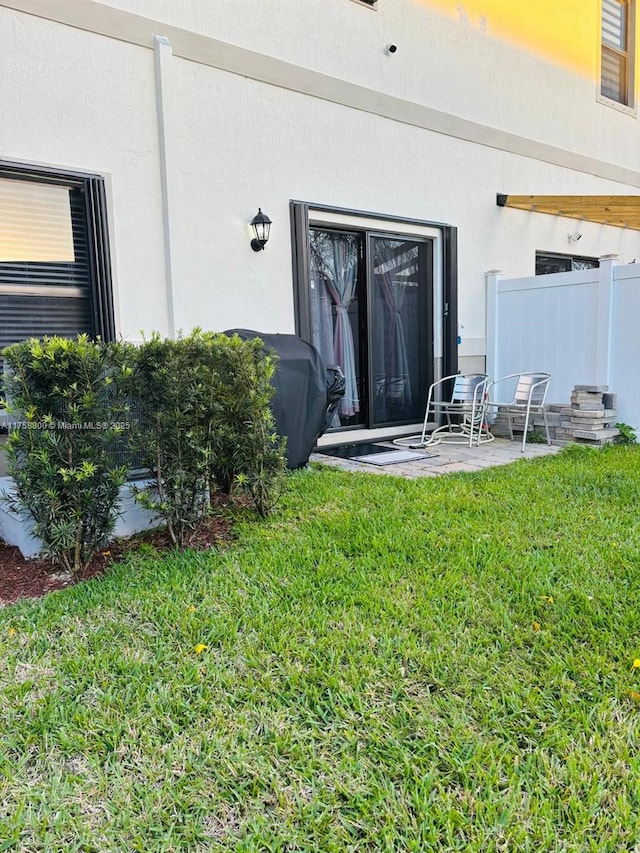 view of exterior entry with stucco siding, a lawn, fence, and a patio