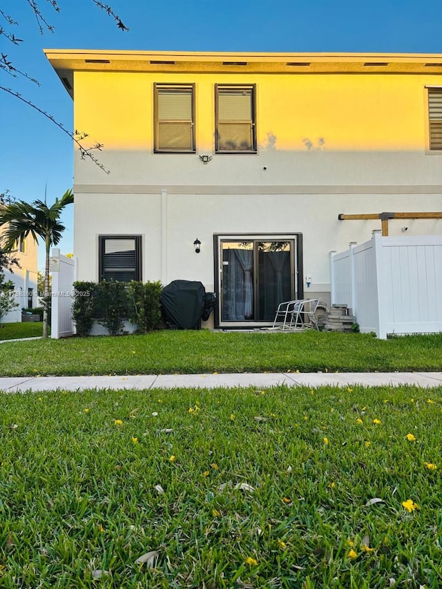 back of house with fence, a lawn, and stucco siding