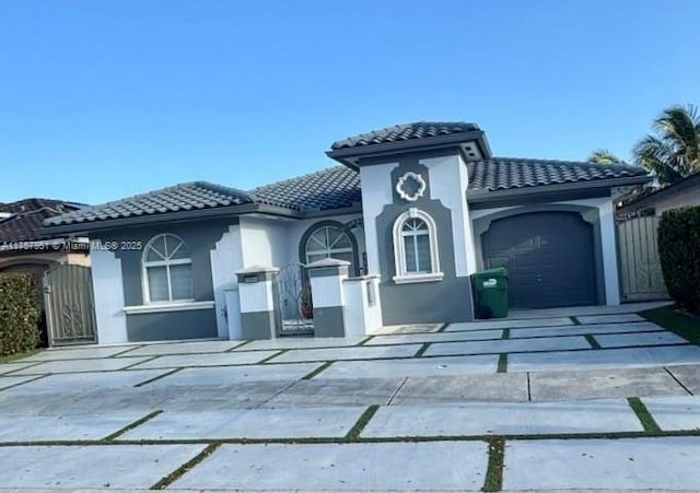 mediterranean / spanish-style home featuring a tile roof, an attached garage, driveway, stucco siding, and a gate