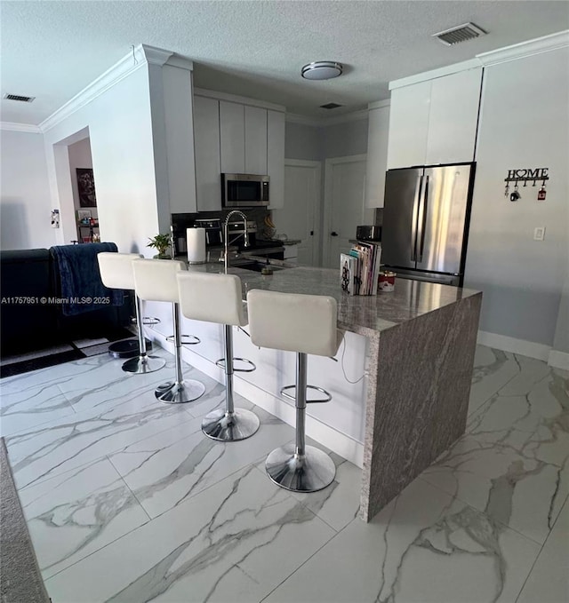 kitchen with appliances with stainless steel finishes, crown molding, marble look tile flooring, a peninsula, and modern cabinets