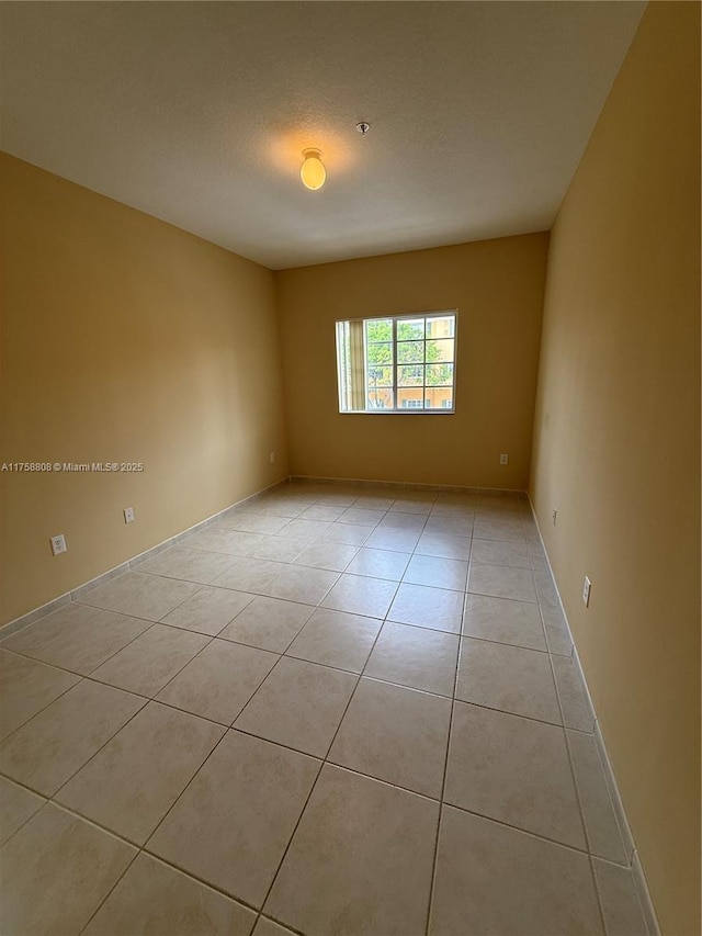 empty room featuring light tile patterned floors, a textured ceiling, and baseboards