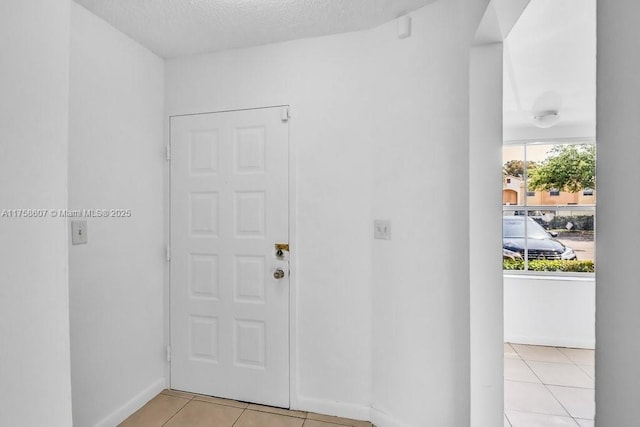 foyer entrance with a textured ceiling, baseboards, and light tile patterned floors