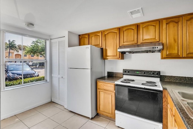 kitchen featuring dark countertops, freestanding refrigerator, light tile patterned flooring, range with electric cooktop, and under cabinet range hood