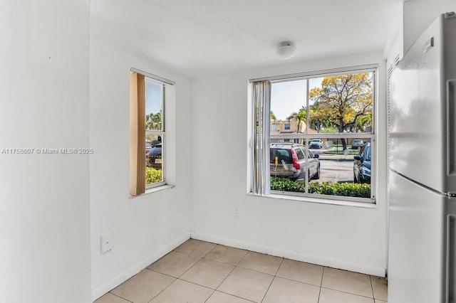 empty room featuring light tile patterned floors, a wealth of natural light, and baseboards