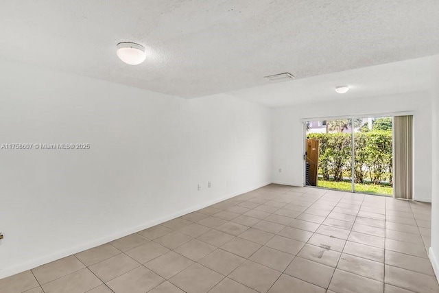 unfurnished room with a textured ceiling, light tile patterned floors, and baseboards