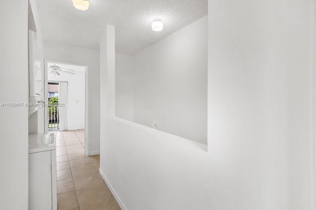 corridor with a textured ceiling, light tile patterned flooring, and baseboards