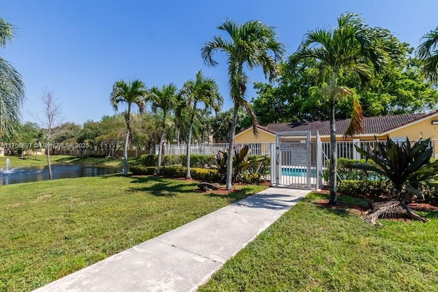 view of community with a water view, a swimming pool, fence, and a yard