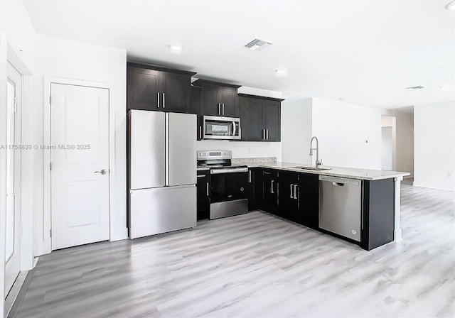 kitchen with visible vents, a sink, appliances with stainless steel finishes, a peninsula, and light stone countertops