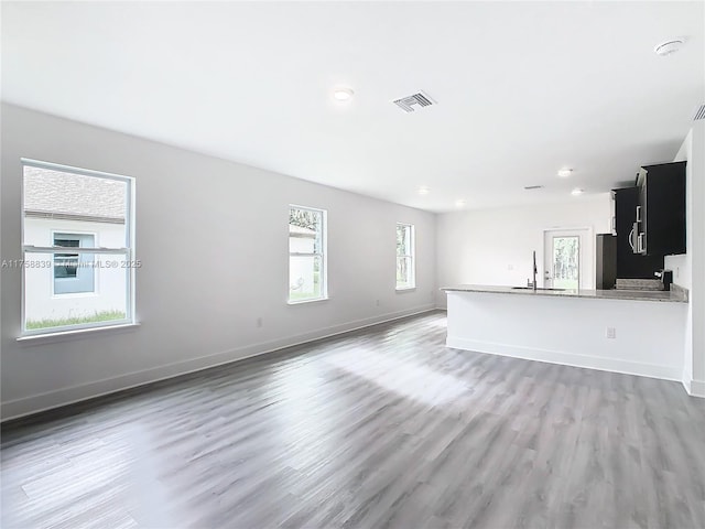 unfurnished living room with light wood-type flooring, visible vents, a sink, recessed lighting, and baseboards