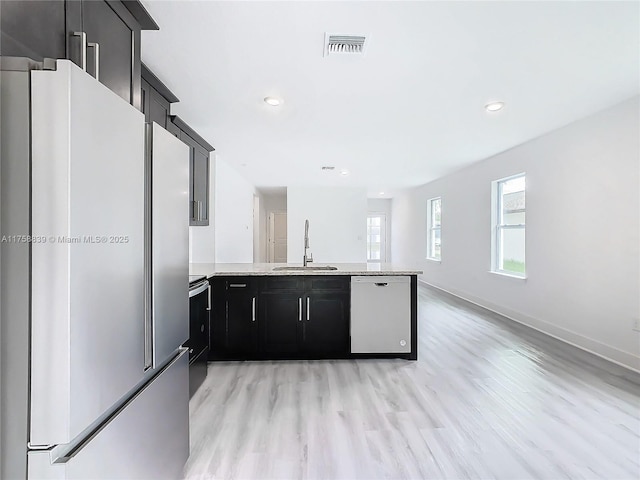 kitchen featuring visible vents, dishwasher, a peninsula, freestanding refrigerator, and a sink