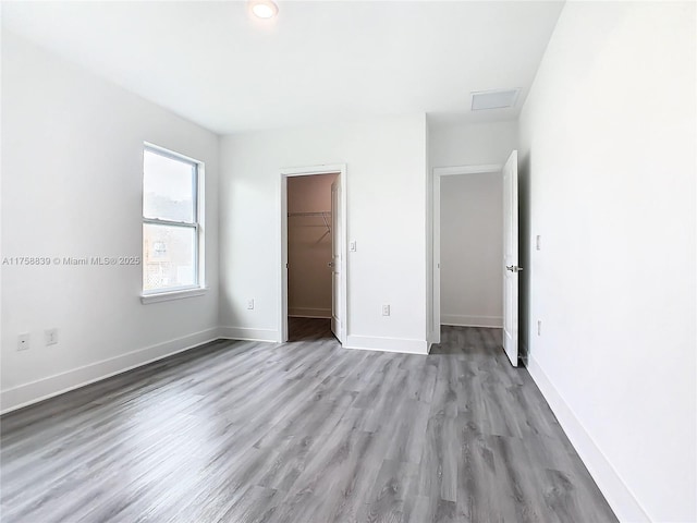 unfurnished bedroom featuring a closet, a walk in closet, baseboards, and wood finished floors