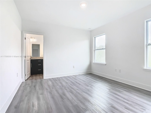 unfurnished bedroom with ensuite bathroom, light wood-style floors, and baseboards