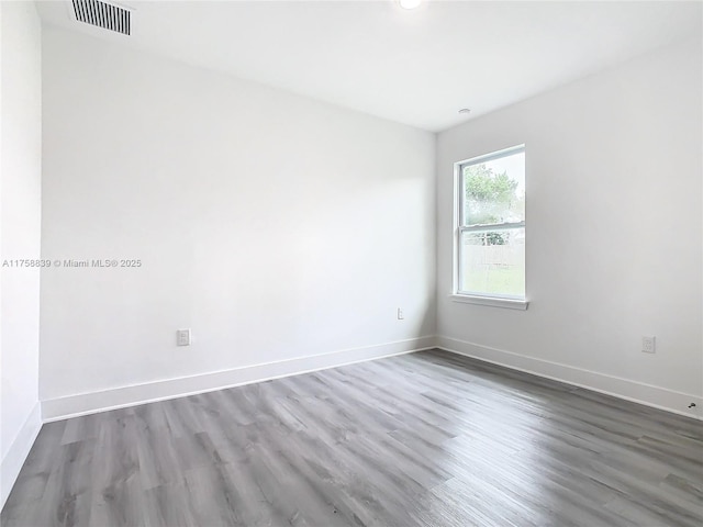 empty room featuring wood finished floors, baseboards, and visible vents