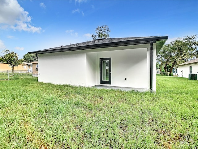 back of property with central AC unit, a lawn, and stucco siding