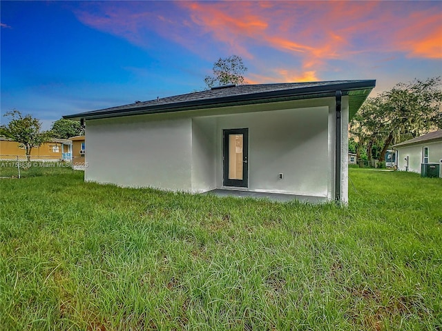 back of property at dusk featuring central AC unit, stucco siding, and a lawn