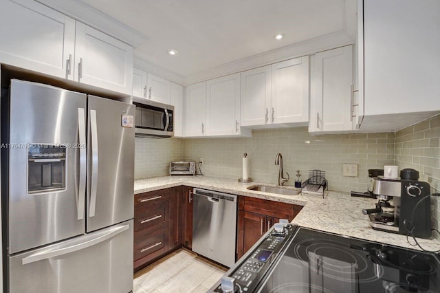 kitchen with light stone counters, stainless steel appliances, backsplash, white cabinetry, and a sink