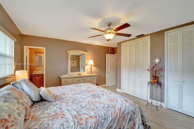 bedroom with a textured ceiling, ceiling fan, visible vents, baseboards, and two closets