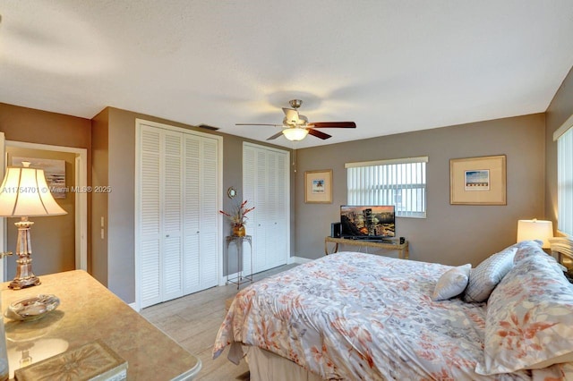 bedroom with ceiling fan, visible vents, baseboards, light wood-type flooring, and two closets