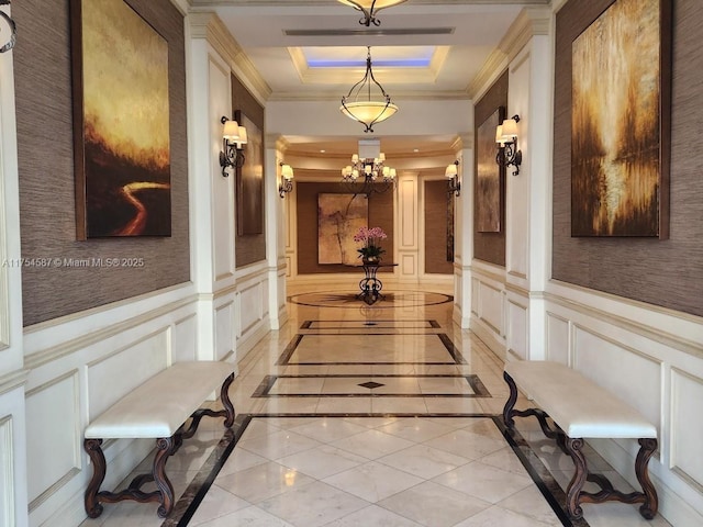 hallway with ornamental molding, a raised ceiling, wainscoting, and a decorative wall