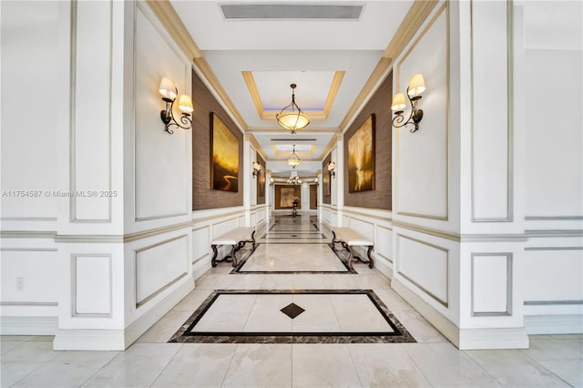 hall featuring a decorative wall, an inviting chandelier, a raised ceiling, and visible vents