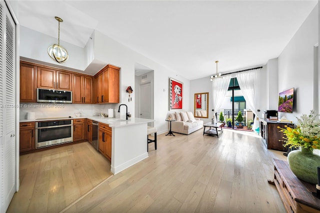 kitchen featuring light wood finished floors, light countertops, appliances with stainless steel finishes, a peninsula, and an inviting chandelier