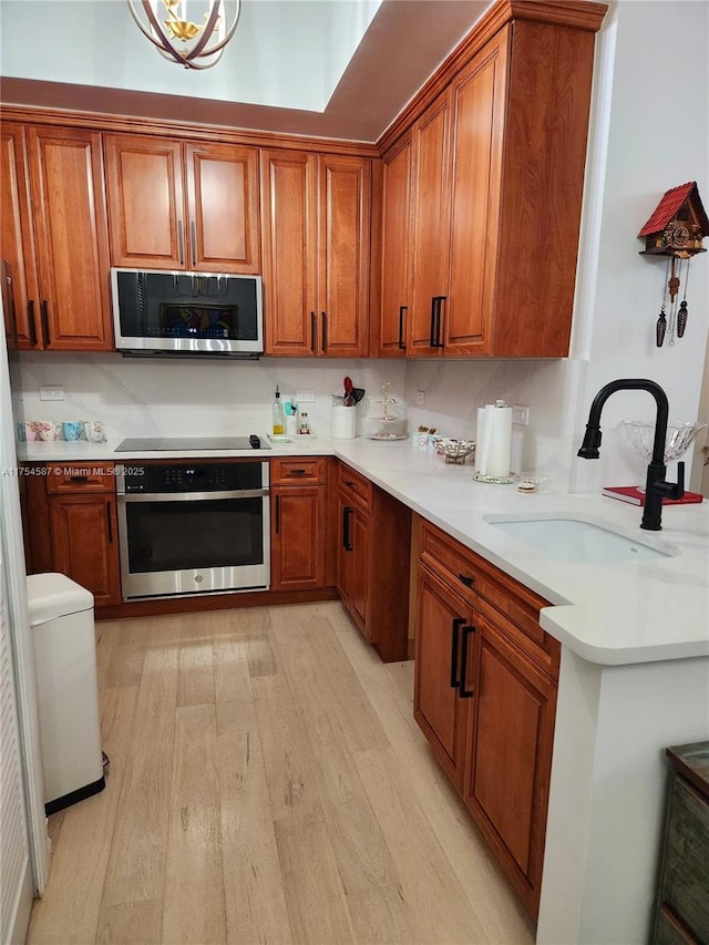 kitchen with appliances with stainless steel finishes, light wood-type flooring, brown cabinets, and a sink