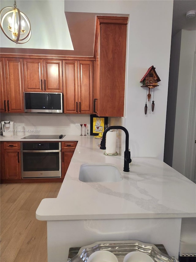 kitchen featuring light wood finished floors, appliances with stainless steel finishes, brown cabinets, a chandelier, and a sink