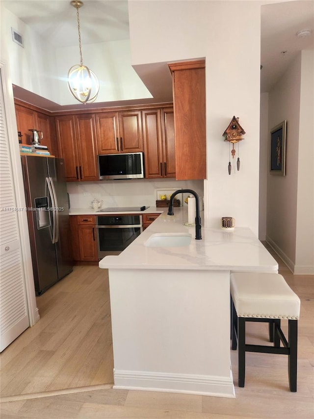 kitchen with brown cabinets, visible vents, appliances with stainless steel finishes, a sink, and a peninsula