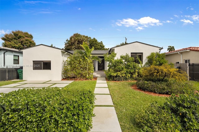 view of front facade featuring fence, a front lawn, and stucco siding