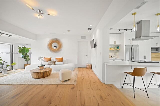 living room featuring light wood-type flooring, visible vents, and track lighting