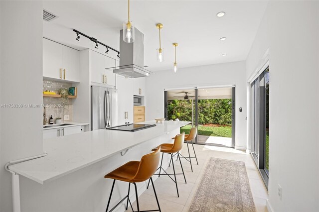 kitchen featuring a breakfast bar, island exhaust hood, stainless steel appliances, white cabinets, and a sink