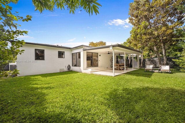 rear view of property with stucco siding, ceiling fan, a lawn, and a patio