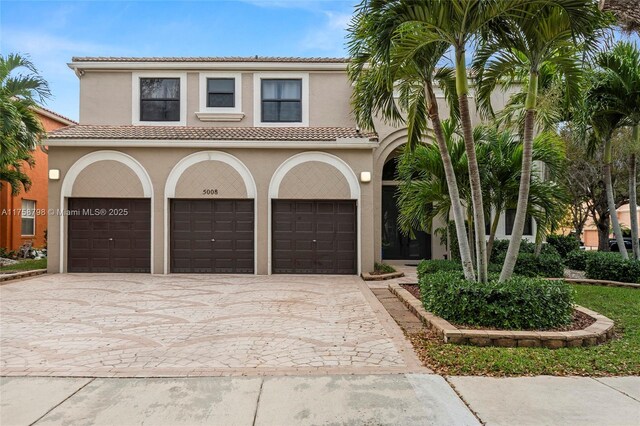 mediterranean / spanish house featuring an attached garage, a tile roof, decorative driveway, and stucco siding