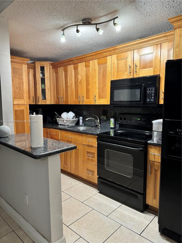 kitchen with light tile patterned floors, a sink, black appliances, dark stone countertops, and glass insert cabinets