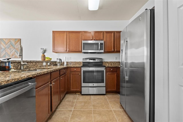 kitchen with dark stone countertops, stainless steel appliances, brown cabinets, and a sink