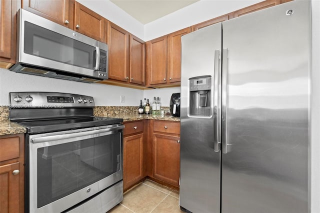 kitchen with stone countertops, brown cabinets, appliances with stainless steel finishes, and light tile patterned flooring