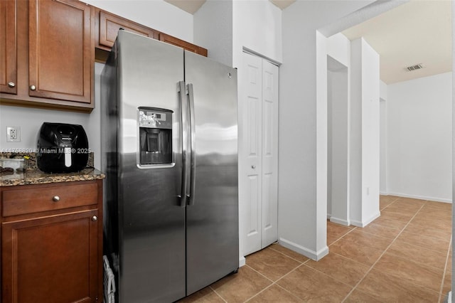 kitchen featuring visible vents, dark stone counters, light tile patterned floors, brown cabinets, and stainless steel refrigerator with ice dispenser