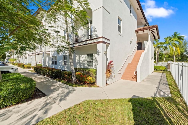 view of side of property with stucco siding, stairs, and fence