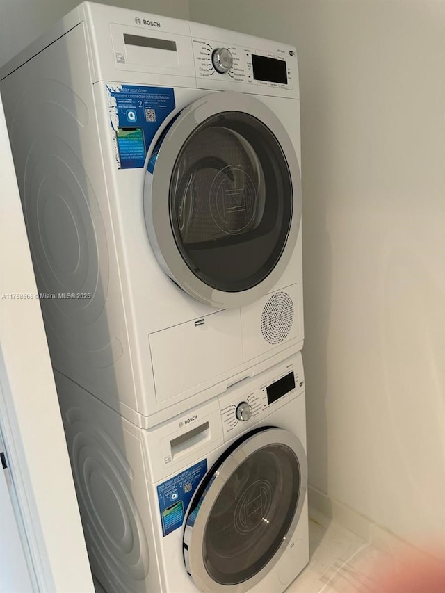 clothes washing area featuring stacked washing maching and dryer, baseboards, and laundry area