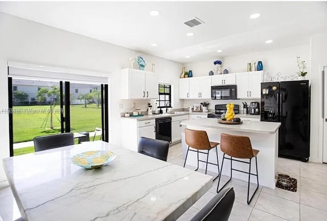 kitchen featuring visible vents, black appliances, a center island, white cabinetry, and a breakfast bar area