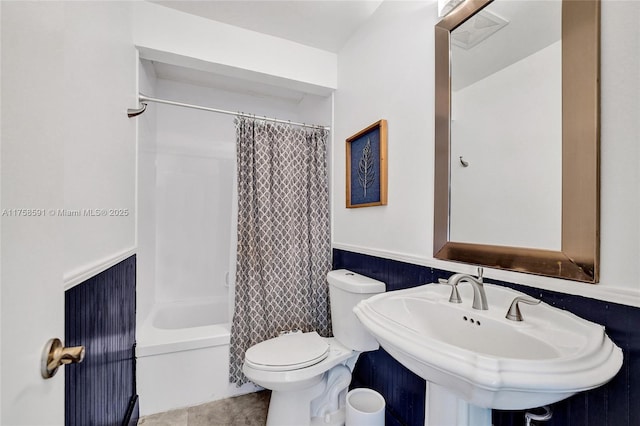 bathroom with shower / bathtub combination with curtain, toilet, wainscoting, a sink, and tile patterned floors