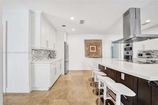 kitchen with island exhaust hood, white cabinetry, a kitchen breakfast bar, and light countertops