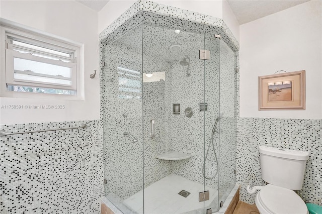 bathroom featuring toilet, a wainscoted wall, a shower stall, and tile walls